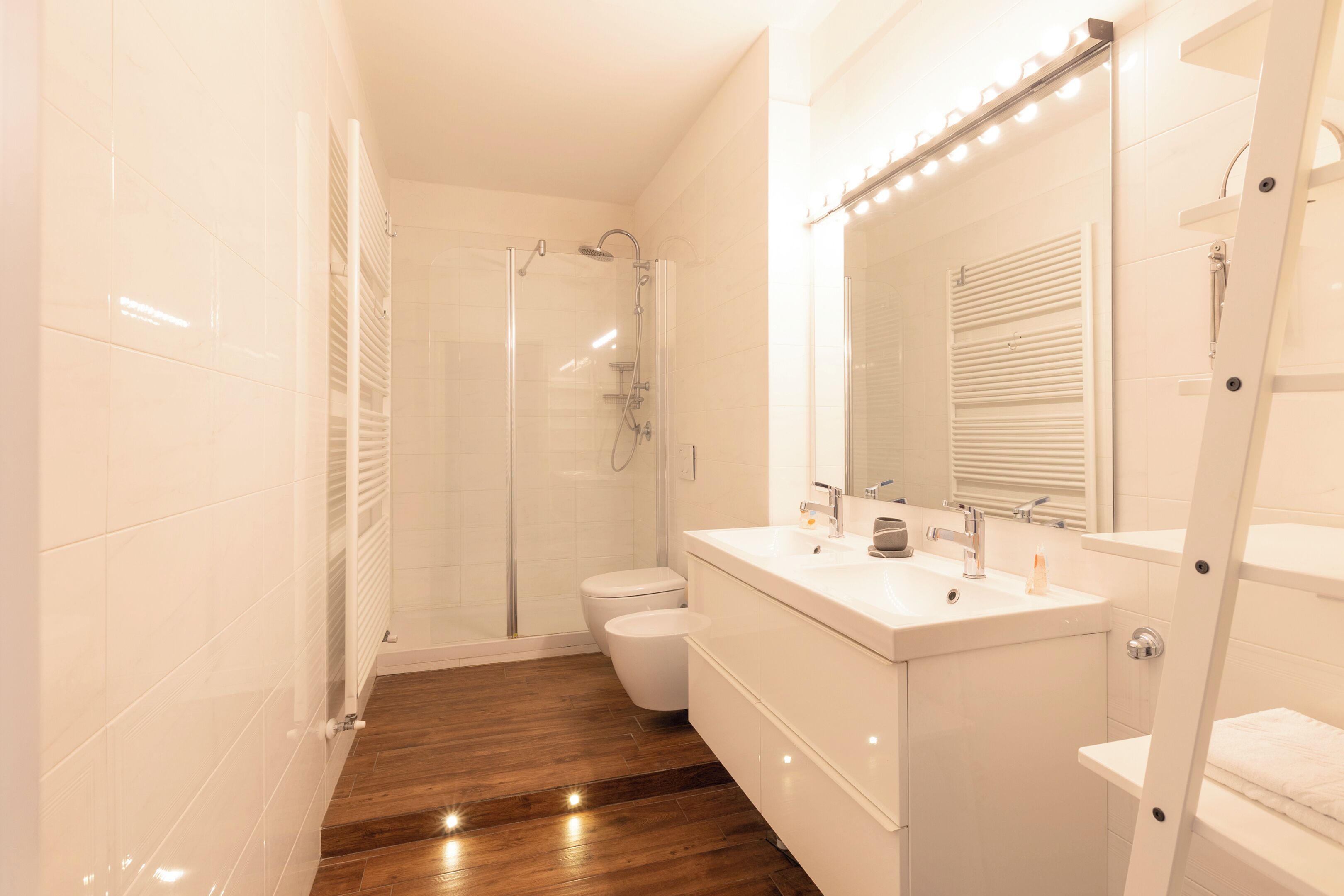Uma casa de banho moderna com chuveiro em cabine de vidro, lavatório branco e toucador com espelho.