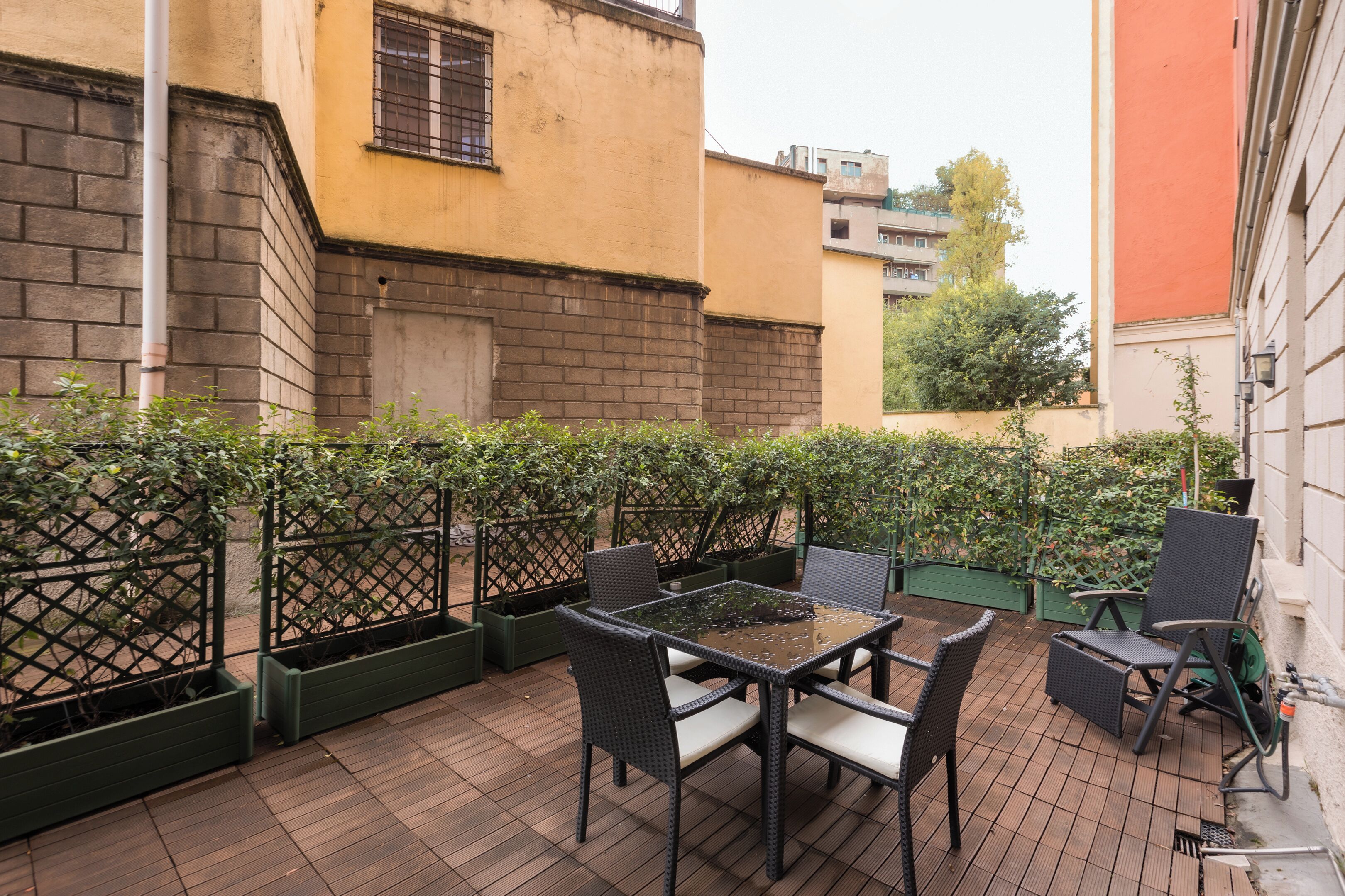 An outdoor patio with a table and chairs, surrounded by a green fence and plants.