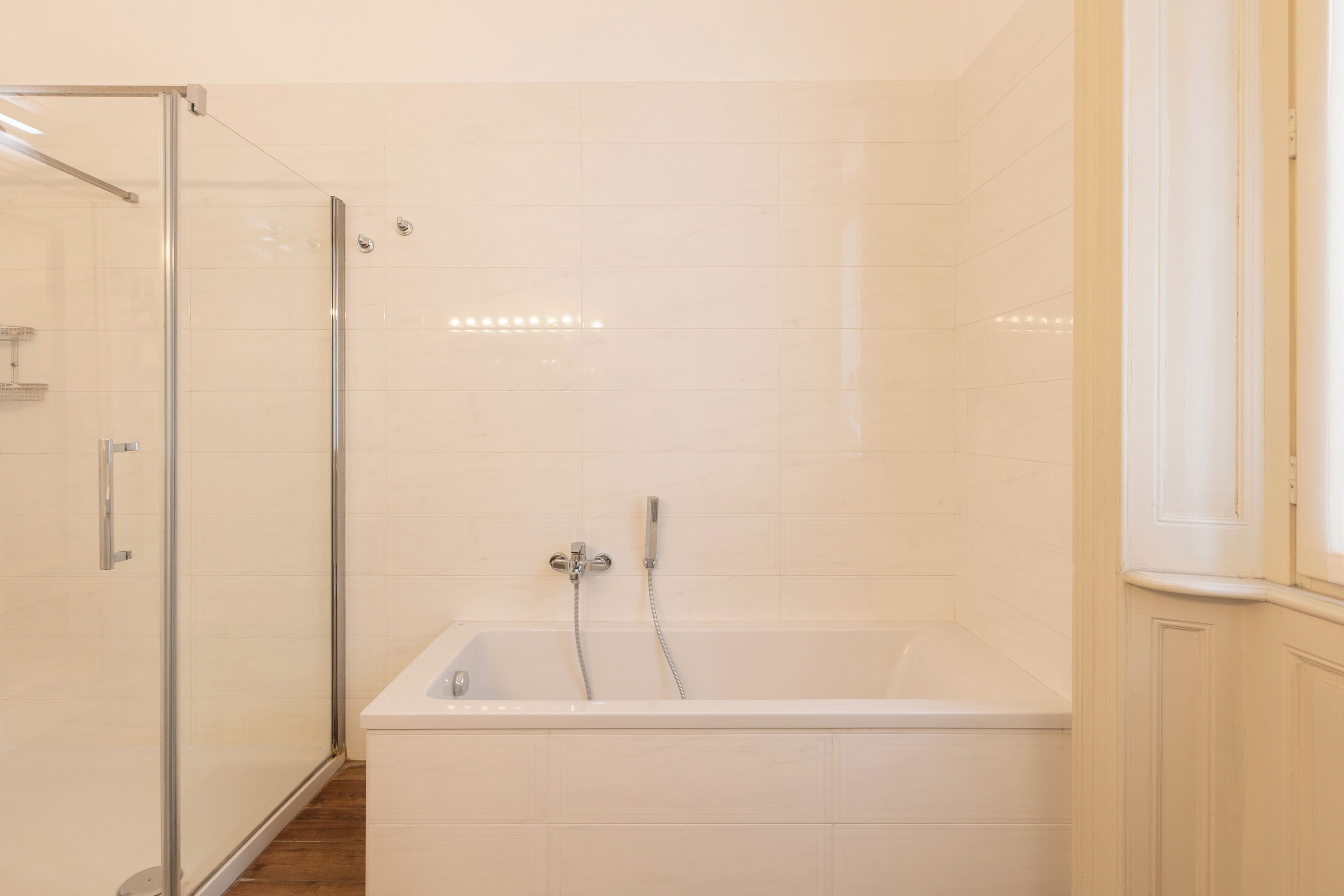 Ein modernes Badezimmer mit einer Glaskabine zur Dusche, einer freistehenden Badewanne und weiß gefliesten Wänden.