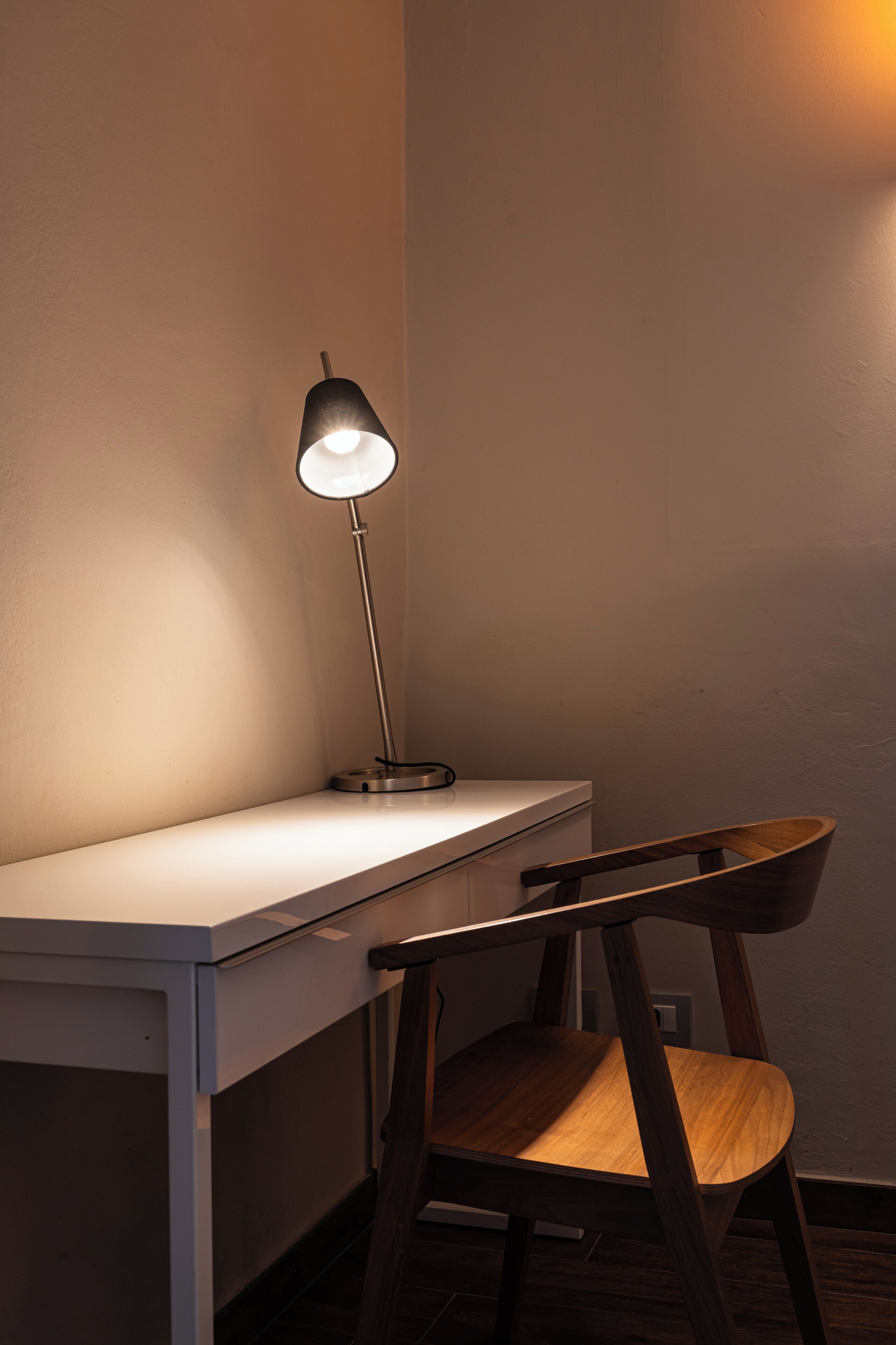 A desk with a lamp, a chair, and a wall.