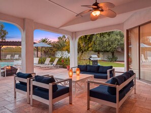 Eine überdachte Terrasse im Freien mit Sitzgelegenheit, Grill und Pool im Hintergrund.