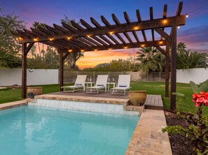 Ein Poolbereich mit einer Pergola, Liegestühlen und Blick auf den Sonnenuntergang.