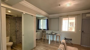 A compact living space with a kitchenette, a small dining area, a shower with a glass door, and a seating area with a sofa and stools. - Hamilton Suites & Appart (Casablanca)