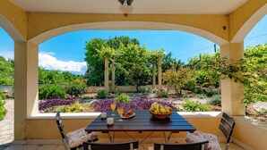 A covered patio with a table set for breakfast, featuring a basket of fruit, a plate of croissants, and a glass of orange juice. - Madonna Field Apartment II - Peaceful 1BR for 3 in Lapad (Dubrovnik)