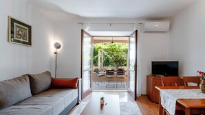 A modern living room with a grey sofa, a wooden coffee table, a TV on a wooden cabinet, and a dining area with a table and chairs. - Madonna Field Apartment II - Peaceful 1BR for 3 in Lapad (Dubrovnik)