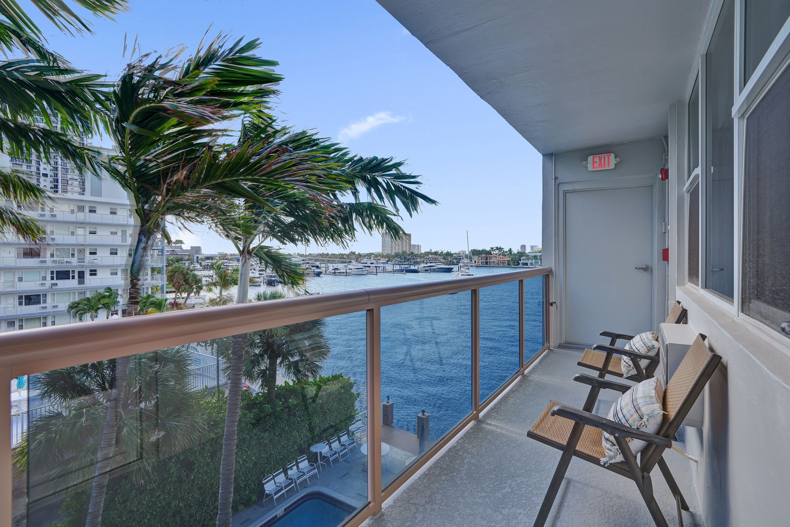 Un balcon avec vue sur l’eau, des palmiers et un bâtiment en arrière-plan.