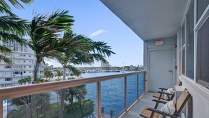 A balcony with a view of the water, palm trees, and a building in the background.