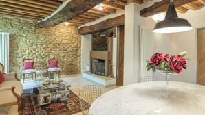 Ein gemütliches Wohnzimmer mit Steinwand, Holzbalken, Kamin und rundem Marmortisch mit Blumenvase.