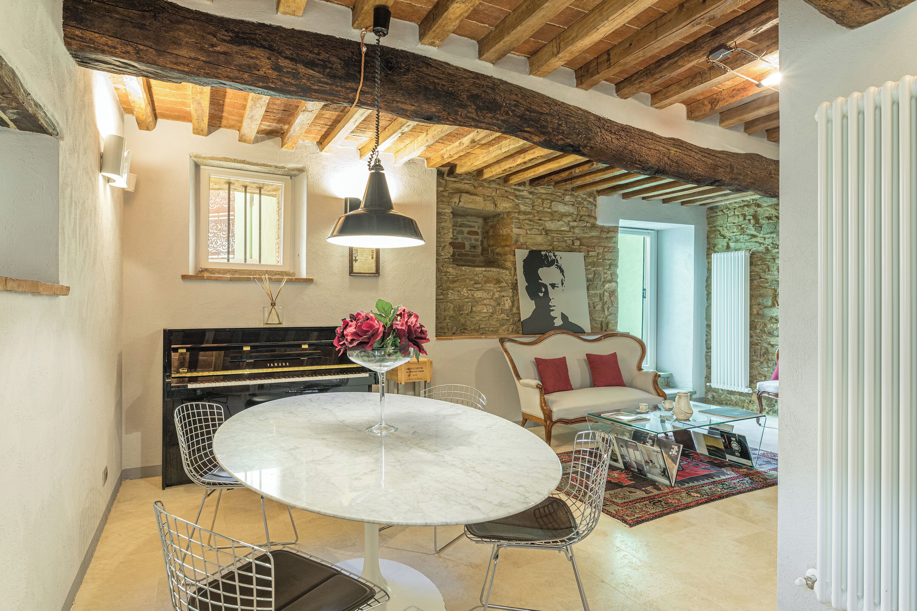 A dining area with a round table, chairs, a piano, and a sofa.