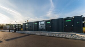 Een rij modulaire slaappods, gemarkeerd met “ROATEL”, met een bord met de tekst “SLEEP WELL”, een beveiligingscontrolepost en een “ROATEL” bord op een gebouw.