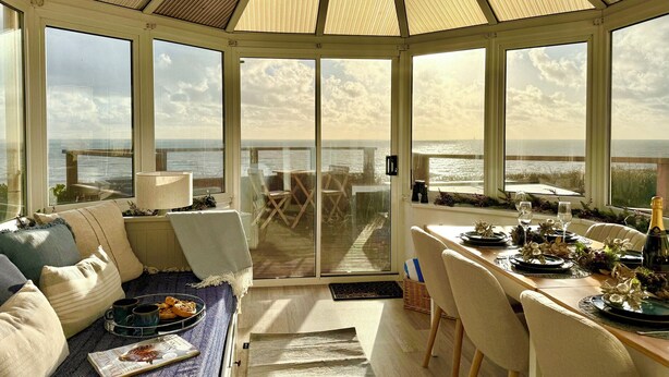 Ein lichtdurchflutetes Zimmer mit Meerblick, ein Essbereich mit Tisch für Zwei und eine gemütliche Sitzecke mit Kissen und einer Auswahl an Gebäck.