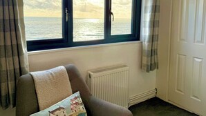 Ein Zimmer mit Meerblick durch zwei Fenster, inklusive Heizkörper, Tür und Sessel mit Kissen.