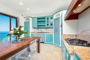 Una cocina moderna con armarios azul turquesa, una mesa de comedor de madera y vistas al mar.