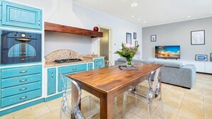 Een moderne keuken met blauwe kastjes, een houten eettafel en een televisie in de woonkamer.