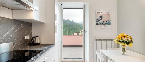 A modern kitchen with a stove, oven, and microwave, a dining area with a table and chairs, and a view of a mountain through an open door.