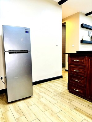 A modern kitchen with a stainless steel refrigerator, wooden flooring, and a dark wooden cabinet. - Entire serviced apartment in Kampala, Uganda (Kampala)