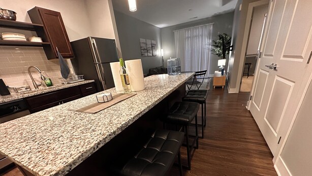 A kitchen with a granite countertop, black bar stools, and a refrigerator.