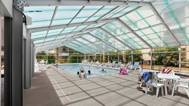A covered swimming pool with clear glass panels, lounge chairs, and a poolside area. - Heron Pointe D5- 2BR- 5 Minute Walk To Beach (Myrtle Beach)