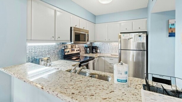 A modern kitchen with white cabinets, a stainless steel refrigerator, a microwave, and a granite countertop. - Kingston Laurel Court 311- 2BR/2BA- Outdoor Pool (Myrtle Beach)