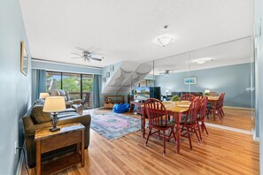 A modern living room with a sofa, a coffee table, and a dining area with wooden chairs and a table. - Kingston Laurel Court 311- 2BR/2BA- Outdoor Pool (Myrtle Beach)