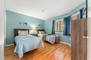 Une chambre avec deux lits, un plancher en bois, une fenêtre avec des rideaux et une porte dotée d’une poignée en laiton.