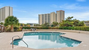 A swimming pool with a metal ladder, surrounded by a landscaped area with palm trees and a hedge. - Kingston Laurel Court 311- 2BR/2BA- Outdoor Pool (Myrtle Beach)