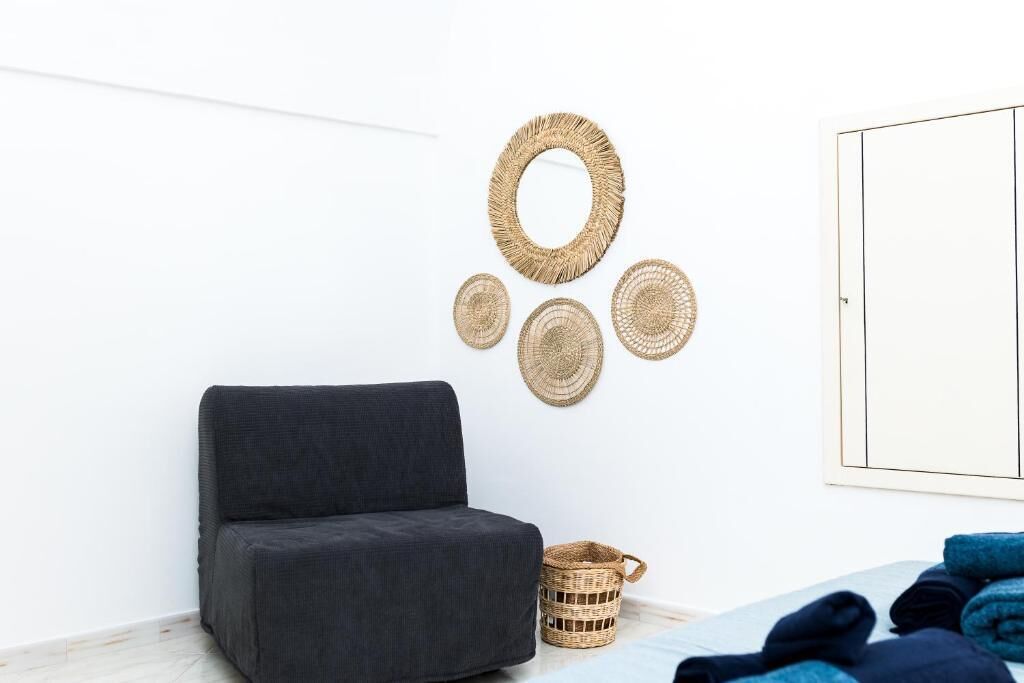 Una habitación con un sofá gris oscuro, un tapiz de pared tejido, una cesta de mimbre y toallas enrolladas sobre la cama.