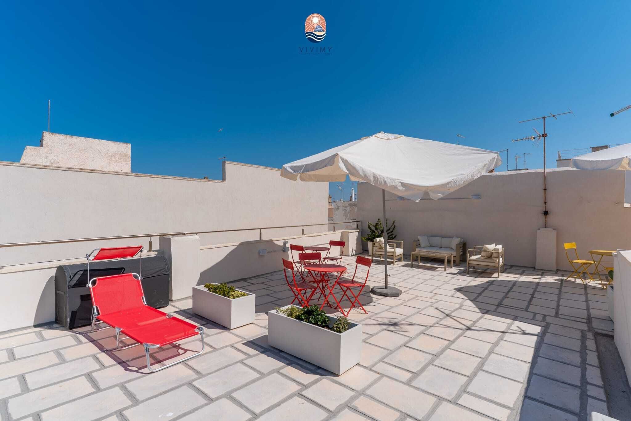 A rooftop terrace with outdoor seating, a grill, and a white umbrella.