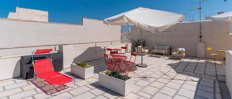 A rooftop terrace with outdoor seating, a grill, and a white umbrella.
