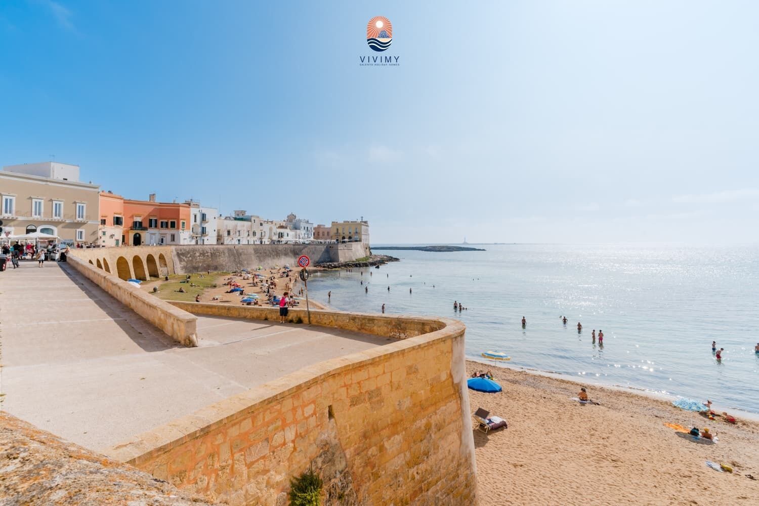 Une promenade en bord de mer, avec un mur de pierre, une plage et des bâtiments en arrière-plan.