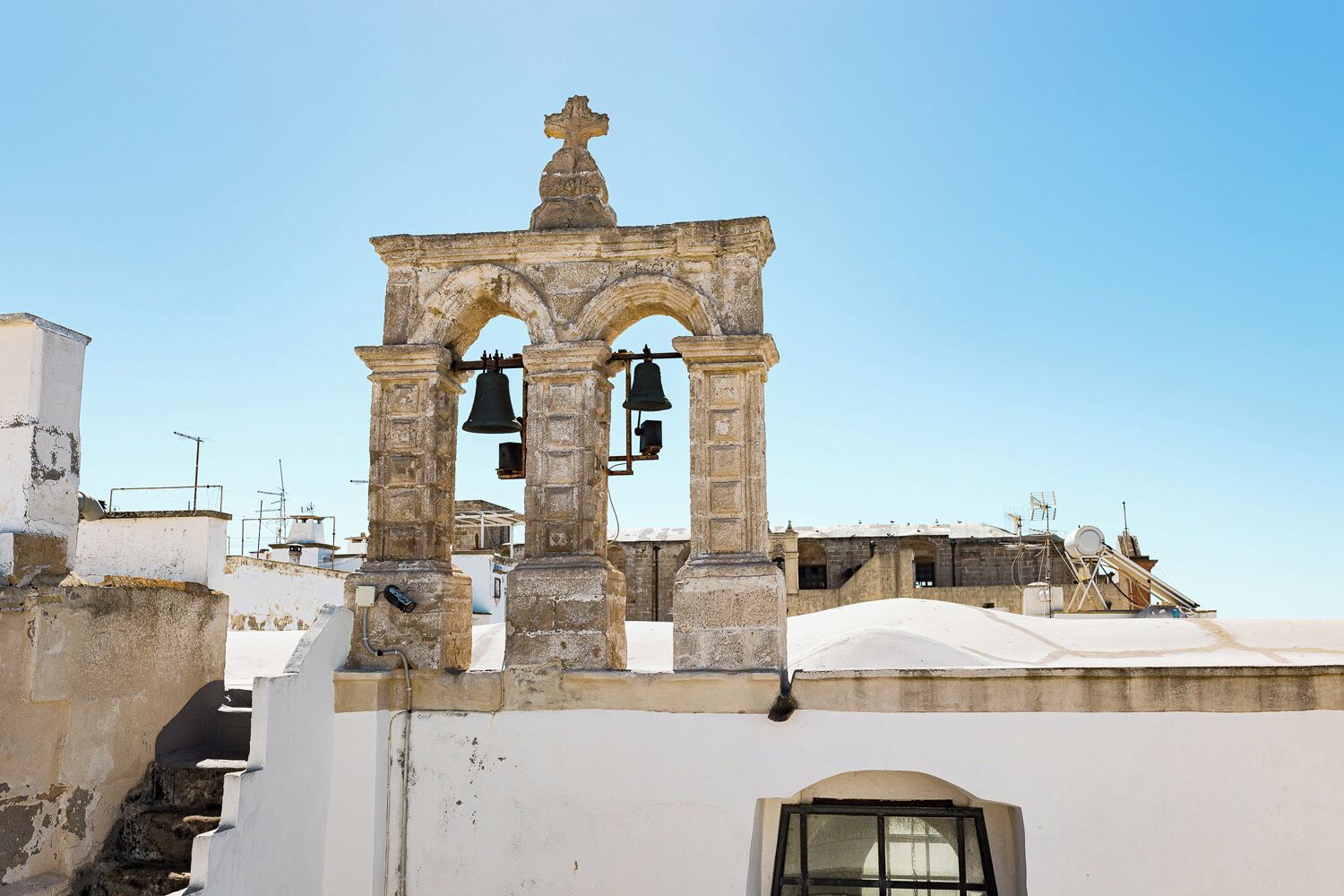 A historic bell tower with a cross on top, surrounded by buildings.