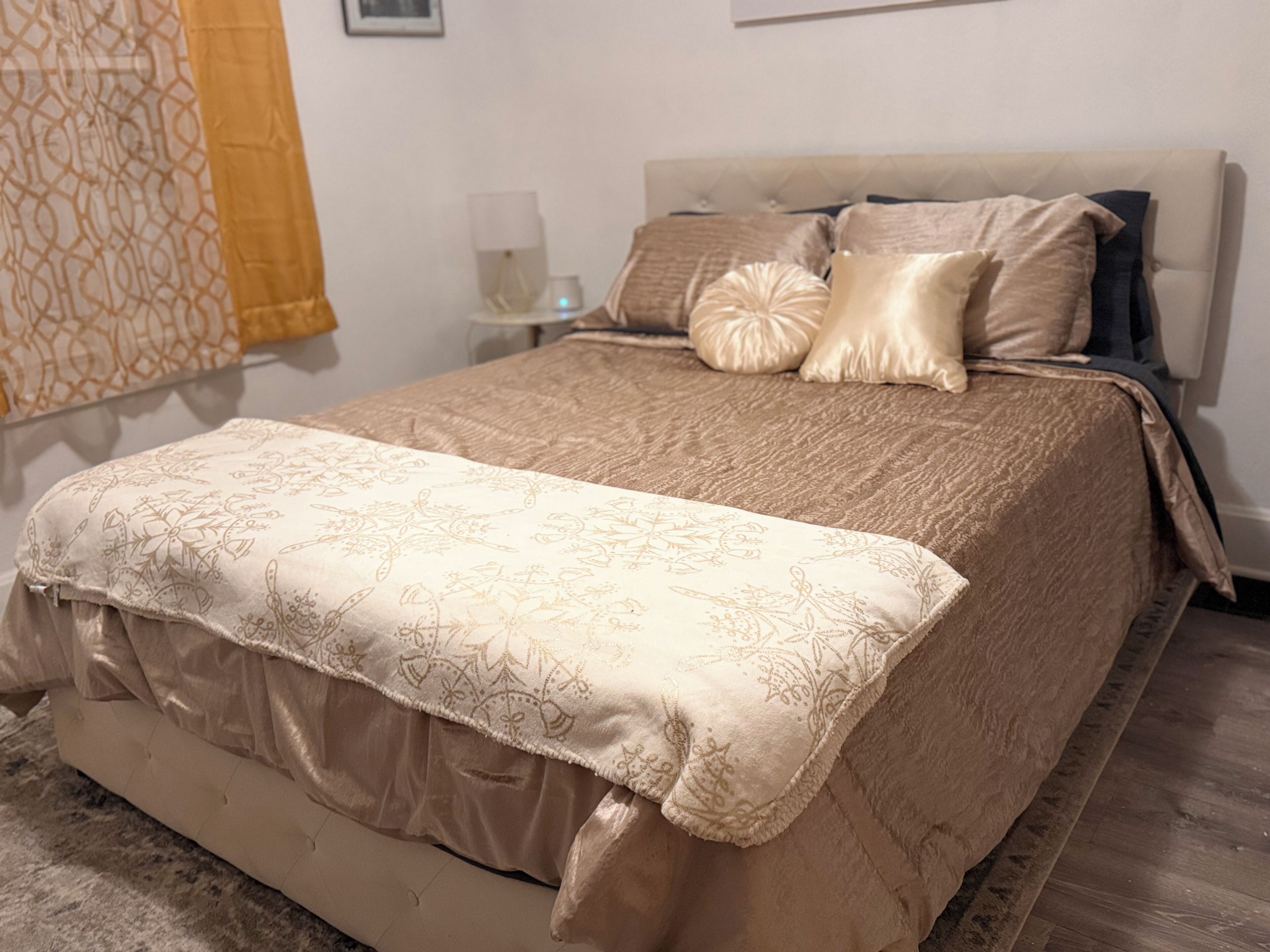 A neatly made bed with a patterned bedspread, a bedside table with a lamp, and a window with a curtain.