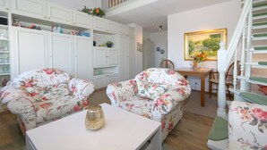 Een woonkamer met bloemenpatroonbanken, een witte tafel en een trap met een leuning.