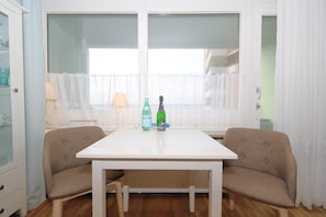 A dining area with a white table, two beige chairs, a bottle of sparkling water, and a bottle of champagne. - House by the sea 035 Wb Sea view (Westerland)
