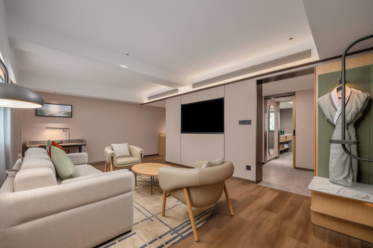 A modern hotel room with a sofa, armchair, TV, and a mirror.