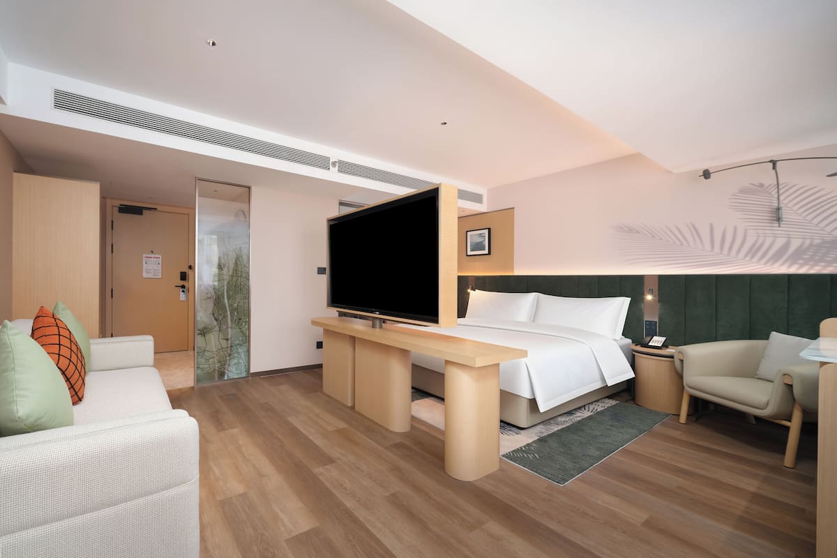 A modern hotel room with a bed, a TV, a desk, a sofa, and a chair.