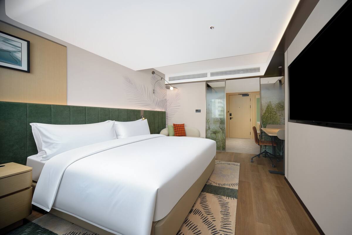 A modern hotel room with a large bed, a desk, and a dining area.