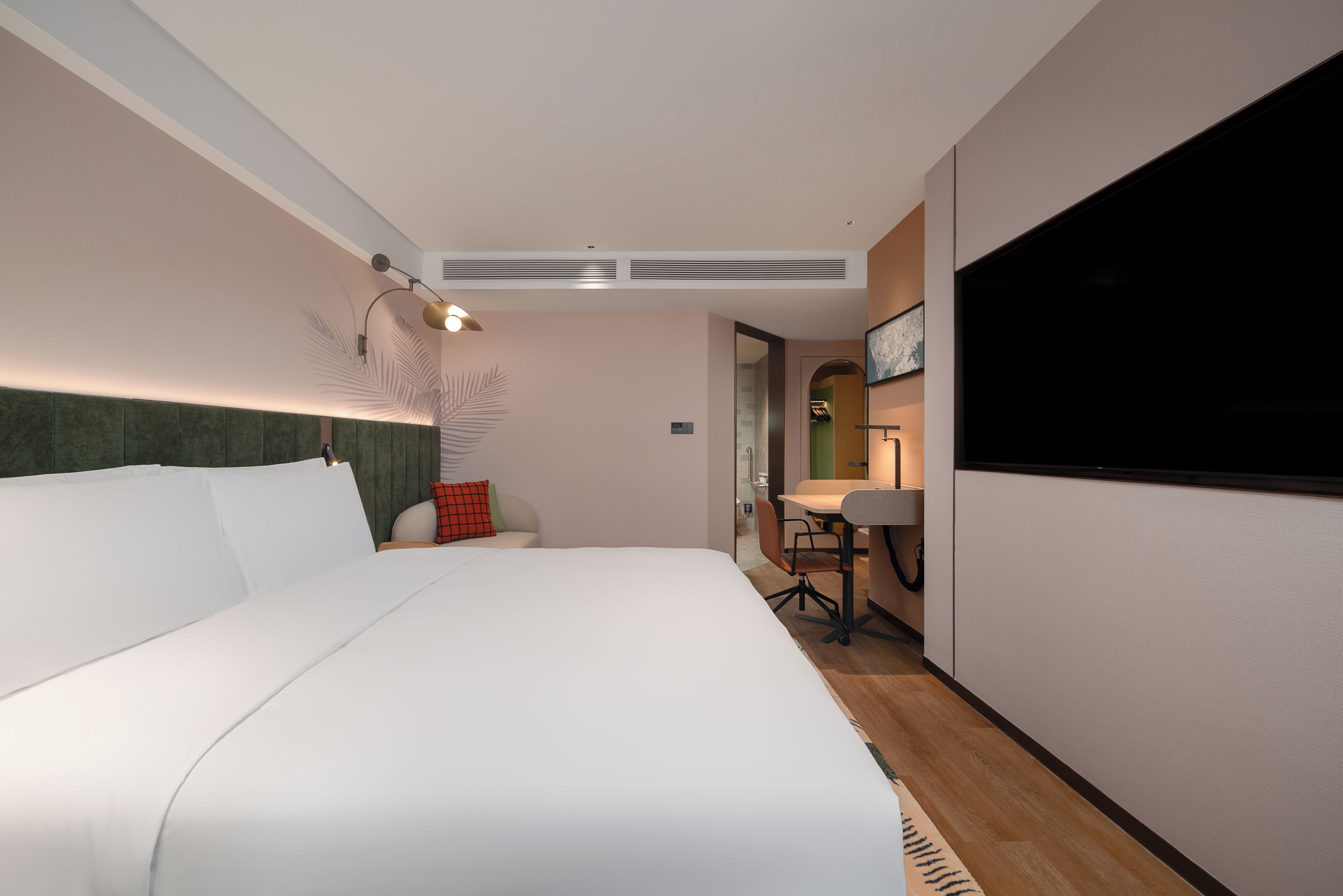 Habitación de hotel con una cama grande, un escritorio con silla, un televisor de pantalla plana y un espejo.