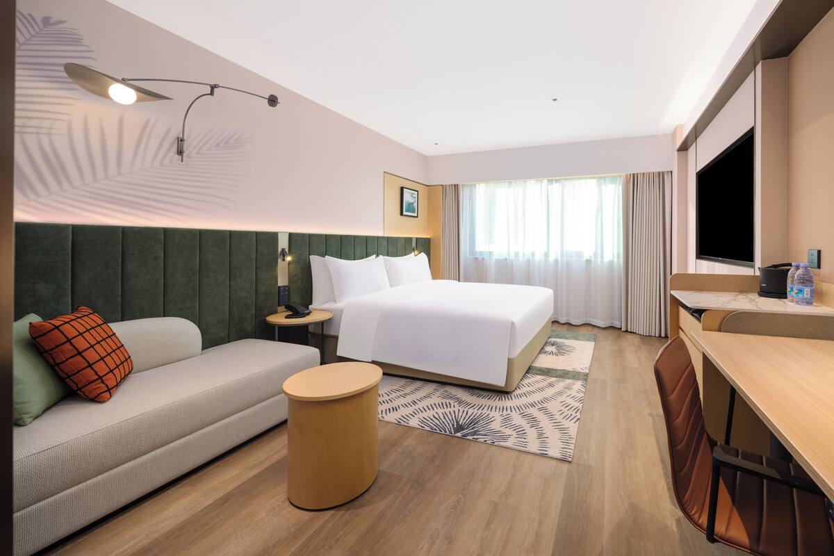 A hotel room with a bed, a sofa, a desk, a lamp, and a TV.