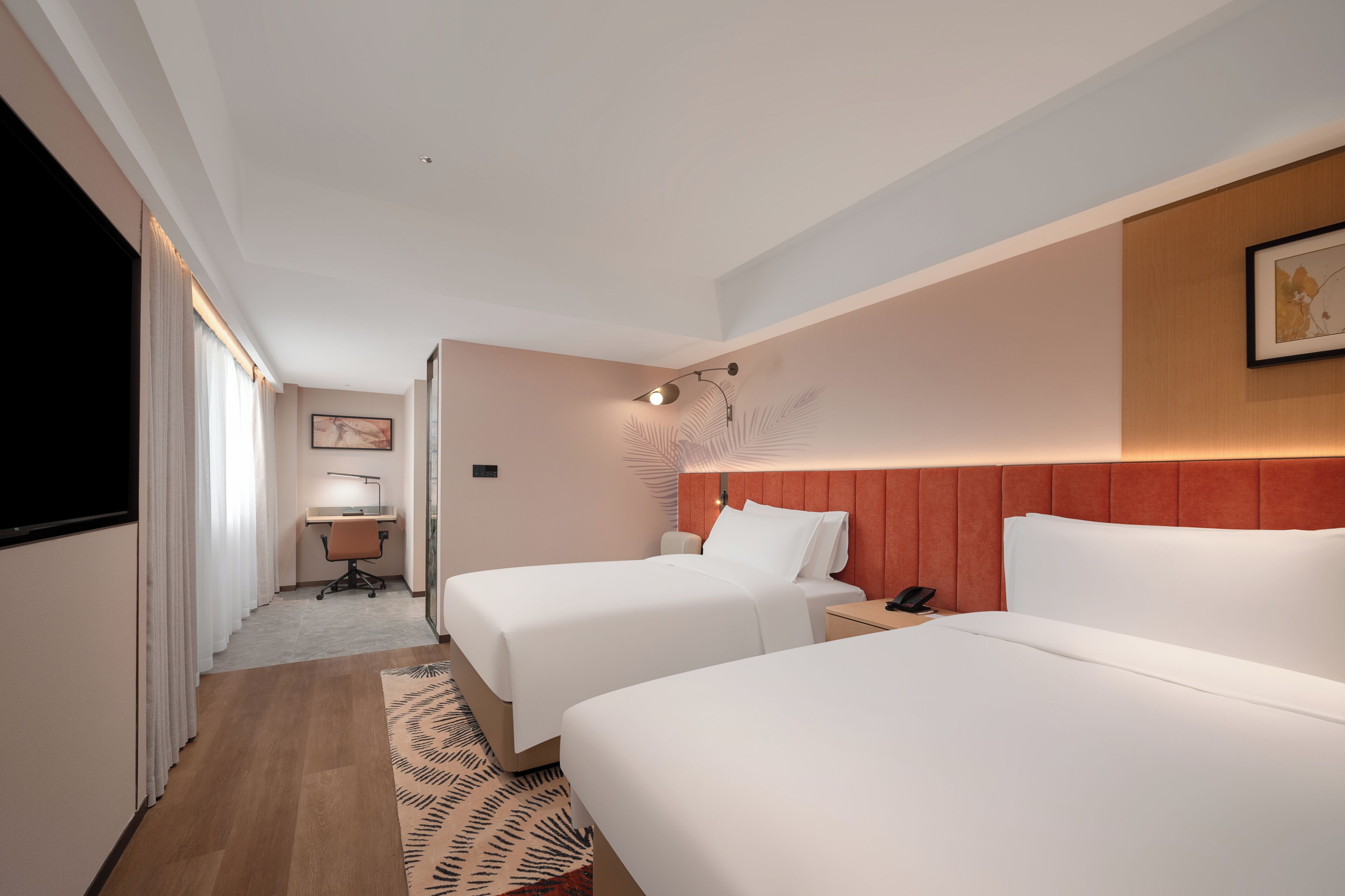 A hotel room with two beds, a desk, a chair, a phone, and a TV.