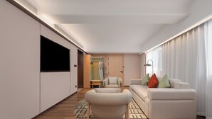 A modern living room with a sofa, armchair, and a flat-screen TV mounted on the wall. - Hilton Garden Inn Shenzhen Luohu Port (Shenzhen)