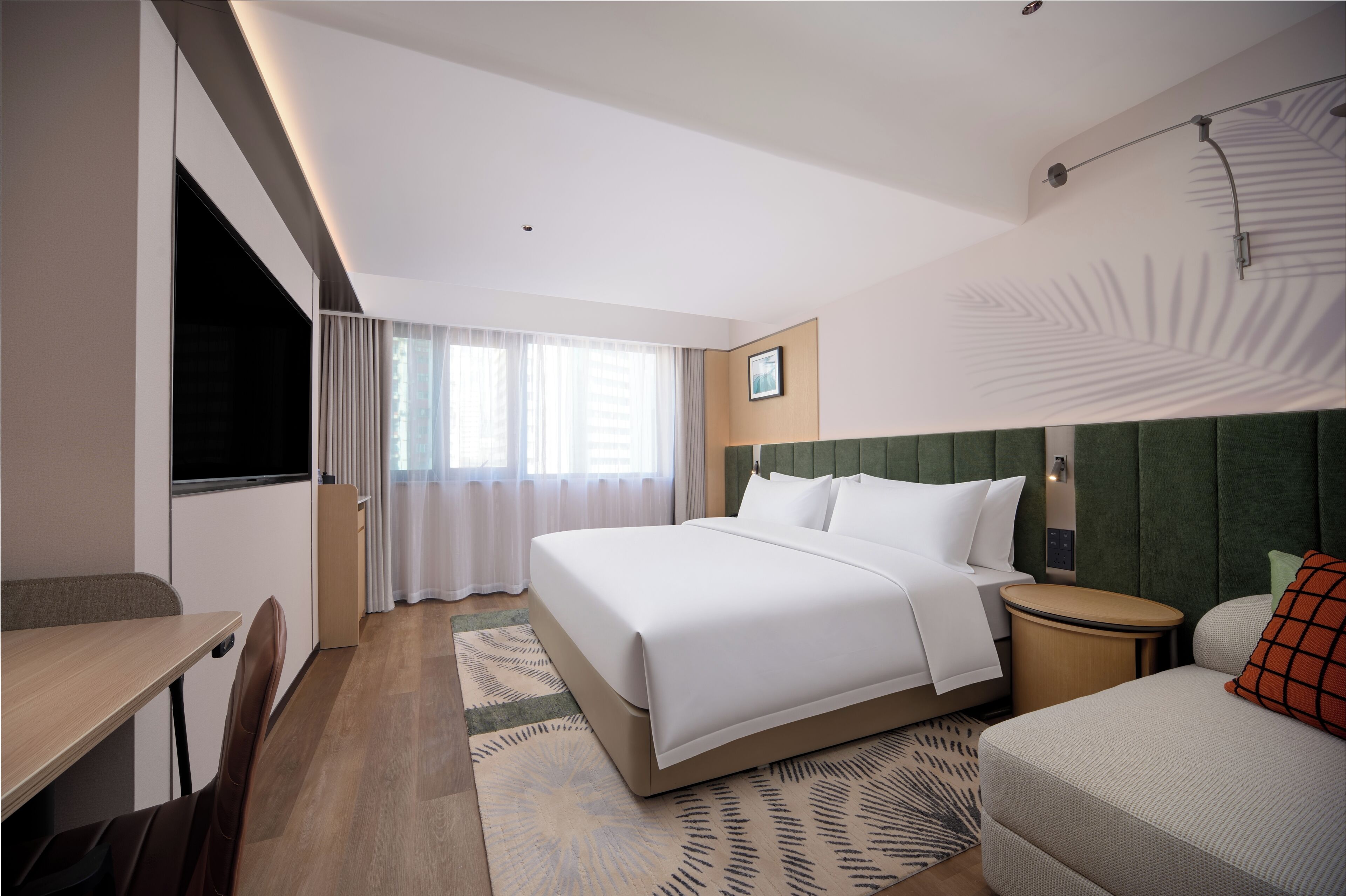 A hotel room with a bed, a desk, a chair, a nightstand, and a window with curtains.