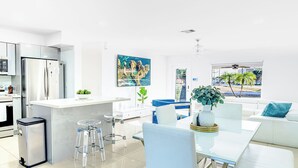 Eine moderne Küche mit Kühlschrank, eine Essecke mit Tisch und Stühlen sowie ein Wohnbereich mit Sofa und Pflanze.