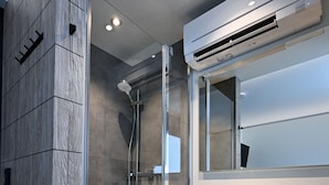 Une salle de bain moderne dotée d’une douche à parois de verre, d’un système de climatisation intégré et d’un grand miroir.