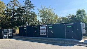 Une rangée de quatre abris de couchage portables de la marque ROATEL, dont l’un est spécialement aménagé pour favoriser un sommeil réparateur, le tout installé sur un fond de verdure, avec des arbres en arrière-plan et un ciel dégagé.