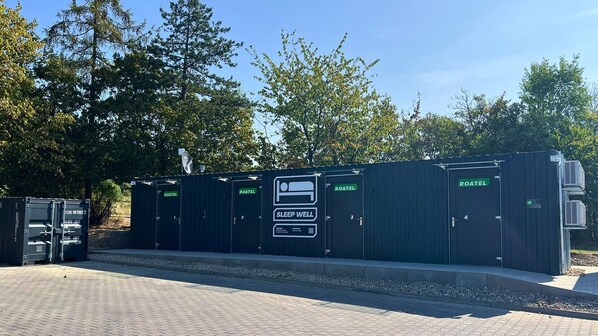 A row of four portable ROATEL sleeping quarters with a designated SLEEP WELL unit, set against a backdrop of trees and a clear sky. - Roatel Wolfhagen A44 (Wolfhagen)