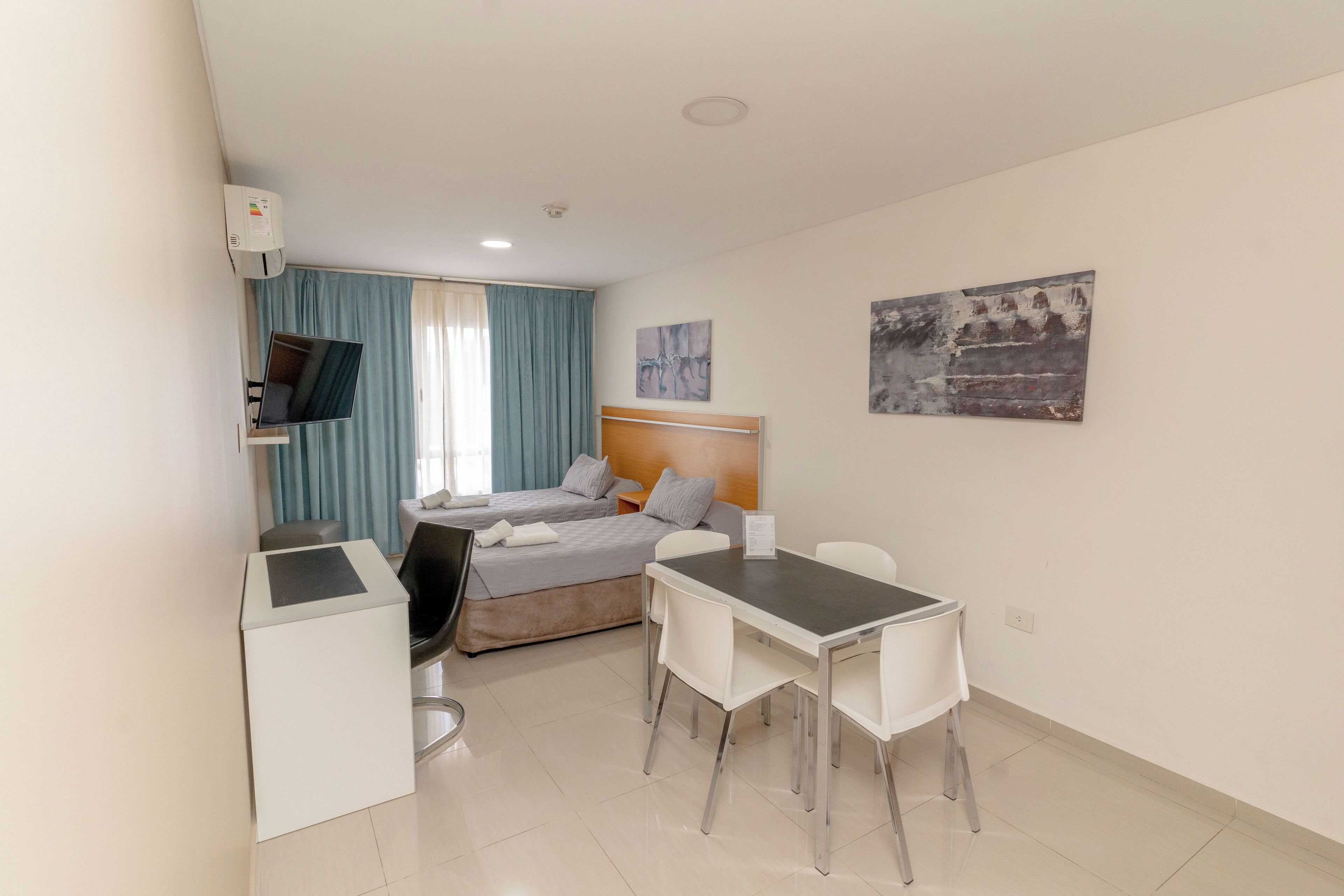 Une chambre d’hôtel avec un lit, un bureau, deux chaises, une télévision et des œuvres d’art accrochées au mur.