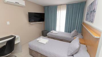A hotel room with two beds, a desk, a TV, and a painting on the wall.
