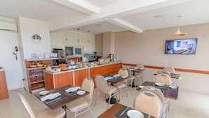 A hotel dining area with tables set for guests, a kitchen in the background, and a television mounted on the wall. - Apart Hotel Illia 121 (Neuquén)