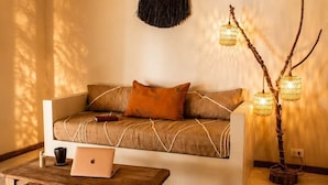 A cozy living room with a sofa, a coffee table, a laptop, a decorative wall hanging, and a unique branch light fixture.